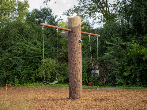 Unique custom playground swing set featuring a natural tree trunk post and chain seats in a green park setting