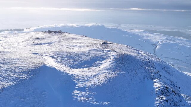 Drone shot over the snow-covered Plynlimon summit, showcasing the rugged surrounding peaks and expansive winter scenery of the Cambrian Mountains in Wales.