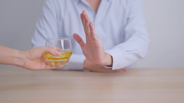 Man making stop hand gesture to refuse a glass of whiskey, Healthy man say no to alcohol drink, stop alcoholism and addiction concept. Responsible man reject a drink before driving and quit booze