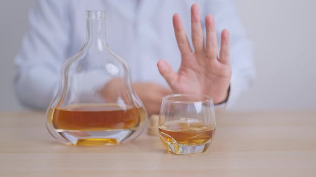 Man making stop hand gesture to refuse a glass of Cognac, Healthy man say no to alcohol drink, stop alcoholism and addiction concept. Responsible man reject a drink before driving and quit booze