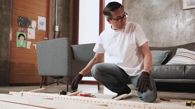 Asian forgetful man self-assembling flat-pack furniture with DIY tools, forgetting and finding wooden dowel joint parts, home improvement, craft installation, hobby workshop, mature active lifestyle.
