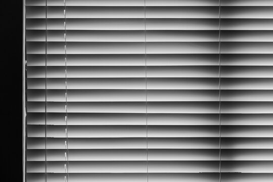Closed horizontal window blinds in black and white create repeating lines, soft gradients and shadow patterns for a minimalist interior, privacy concept, architectural detail, or abstract backgrounds