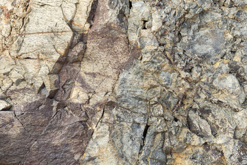 Close-up view of a layered rocky cliff wall featuring varied stone textures, visible cracks and...