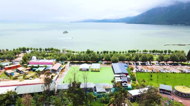 Aerial drone view of Dianchi Lake in Kunming with lakeside amusement park, green fields, parked cars, and boats on water