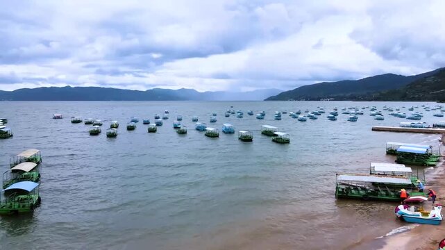 Colorful pedal boats moored along the shoreline of Dianchi Lake in Kunming, Yunnan, with misty mountains and overcast sky in background