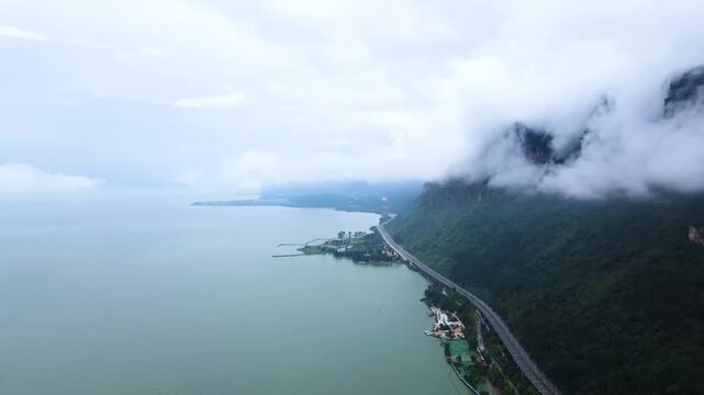 Aerial drone view of Dianchi Lake in Kunming, Yunnan, with mist-shrouded mountains, lakeside highway, and green shoreline infrastructure