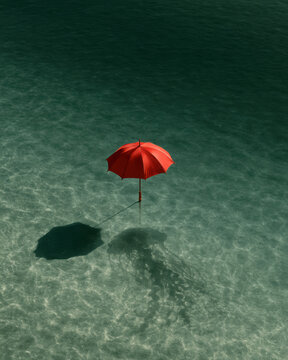 Bright red umbrella standing alone in shallow green water, casting dramatic shadows in a surreal minimalist scene with abundant copy space.