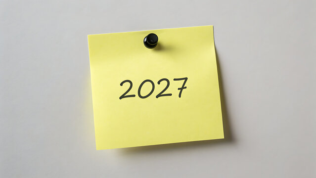 Yellow sticky note with 2027 written on it pinned to a grey wall