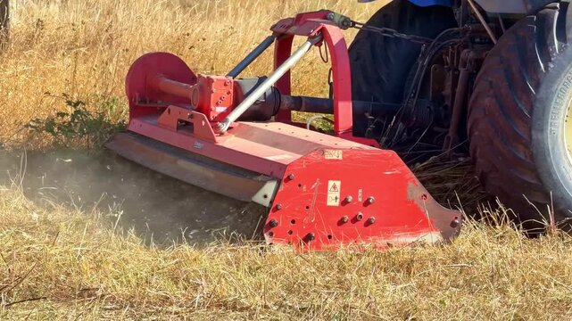 Tractor reverses and turns while a rear-mounted flail mower cuts dry grass, throwing dust and vegetation across a summer field.