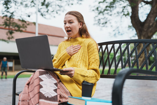 Young woman reacting with surprise using laptop in park