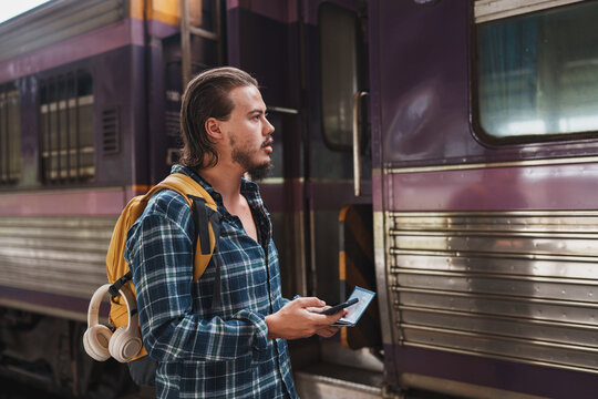 Young traveler waiting for train, holding passport and smartphone