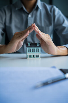 Asian businessman holding hands protect house model, home insurance concept