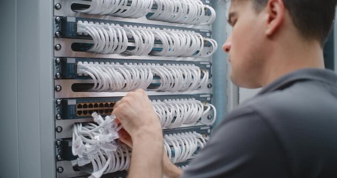 Male Network Technician Performs Physical Layer Cable Patching Inside Server Rack, Adjusting Ethernet Connections and Cable Routes to Support Organized Infrastructure and Network Reliability.