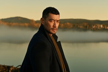 Fototapeta premium Man stands by misty lake, gazing into distance