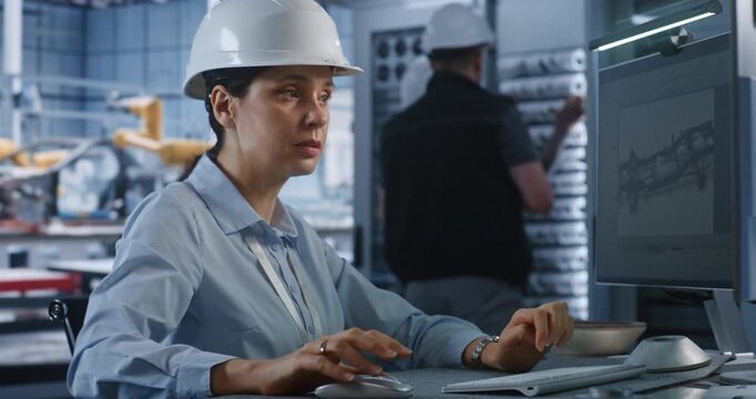 In Modern Smart Plant, Female Professional Engineer in Hardhat Types on PC to Edit 3D Car Chassis Blueprint. Advanced CAD Software and Server Infrastructure Optimize Industry 4.0 Car Production.