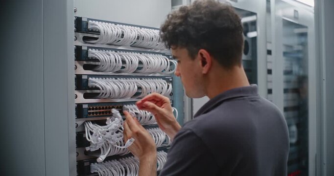 Male Data Center Engineer Connects RJ45 Ethernet Patch Cords to Network Switch, Organizing Cable Bundles Through Rack Managers to Maintain Structured Cabling, Clean Routing and LAN Connectivity.