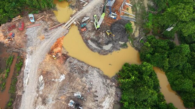 High-angle aerial drone footage showcasing bridge construction, river crossing works, crawler crane, and heavy equipment at an active infrastructure development site.