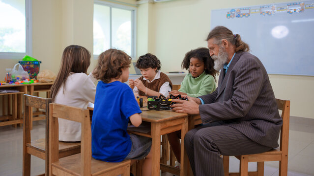 Senior male teacher helping diverse group of young students assembly a robotic kit during a stem science class in classroom school
