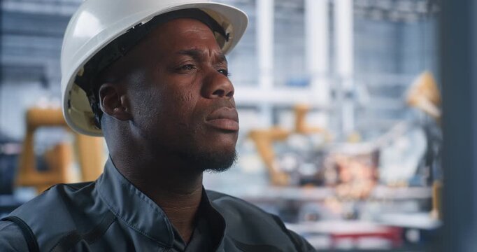Close Up of African American Male Operator at High Tech Modern Control Desk, Supervises Automated Robotic Welding Via Computer Interface. Concept of AI Manufacturing, Industry 4.0 and Robotization.