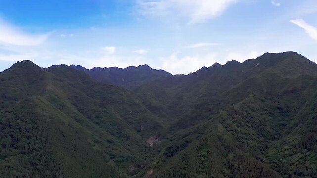 Qinling Mountains aerial drone footage showing lush green forested ridges, deep valleys, and distant rural settlements under partly cloudy sky