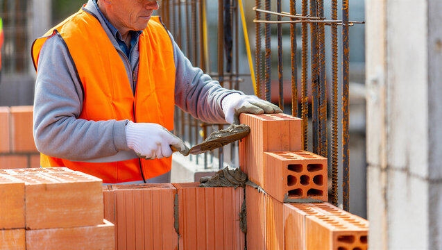 Construction worker installing bricks with trowel at building site construction bricklayer