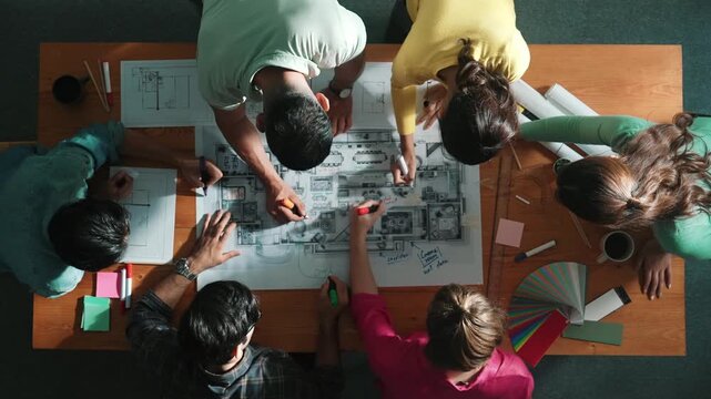 Top down view of civil engineer team writing at blueprint at meeting table with color palettes. Group of diverse people planning and taking a note while manager looking at project plans. Symposium.