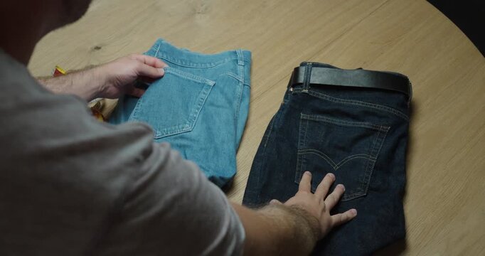 Person comparing light and dark denim jeans side by side while inspecting color, fabric and overall garment quality.