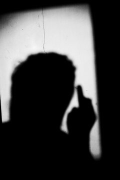 Close up black and white shadow of portrait a man with middle finger hand gesture on the dirty wall