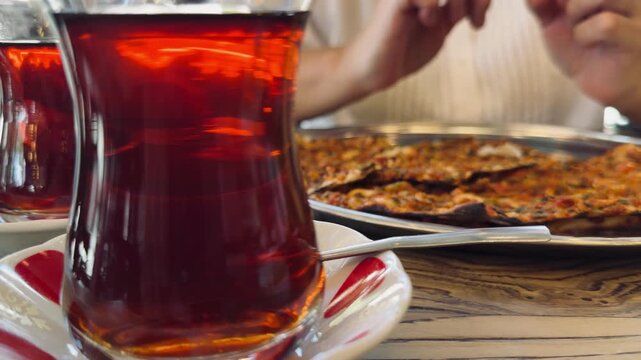 Close up of traditional Turkish tea in authentic tulip glass armudu with national meat pide lahmacun pizza on wooden table, oriental hospitality and local food culture concept in Istanbul, Turkey.