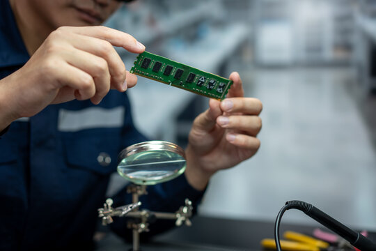 Close-up of an electronics technician inspecting a green memory module with a magnifying glass at a workbench in a repair workshop.