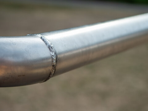 Close-up of a welded joint on a stainless steel tube, showing the visible weld bead and curved metal connection used in railing, fabrication and structural metalwork.