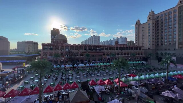 Urumqi Starlight Night Market food street bustling with vendors and diners under clear blue sky at golden hour