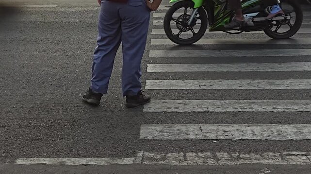 A person stands on a pedestrian crosswalk while a green motorcycle waits nearby on the asphalt road.