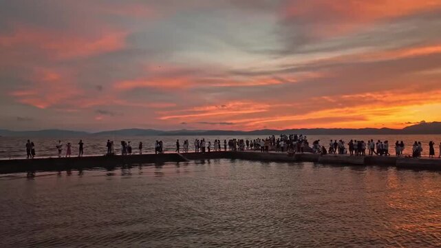 Crowd of people watching sunset from a concrete breakwater at Dianchi Lake in Kunming, Yunnan, with vibrant orange and pink sky reflecting on water