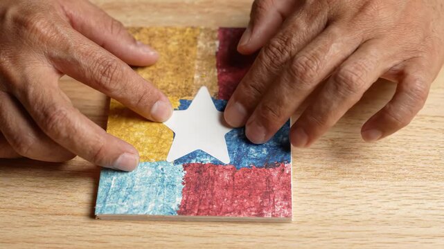 Hand Applying Star Sticker to Handmade Paper Zine Cover, Colorful Collage Craft Process on Wooden Table with Tactile Creative Design Work