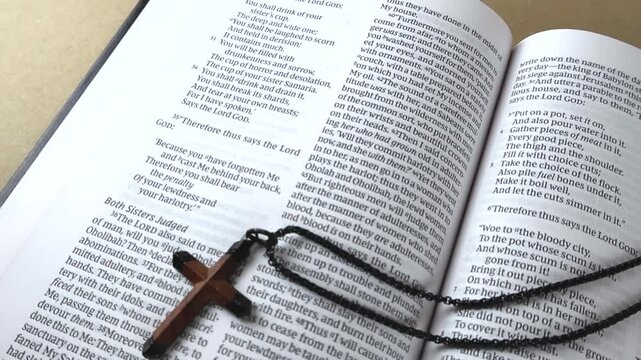 Christian wooden cross necklace resting on the pages of an open Holy Bible, symbolizing faith, devotion, and religious belief. The scripture from the book of Ezekiel is visible in the background
