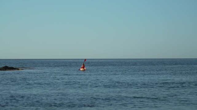 Kayak ocean paddling woman in orange kayak near coastal rocks enjoying summer water sport adventure
