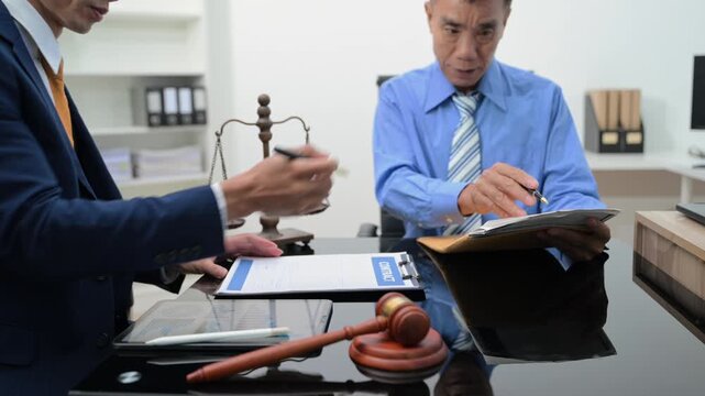 Professional lawyer advising a client, reviewing a contract and financial documents in a modern office with scales of justice