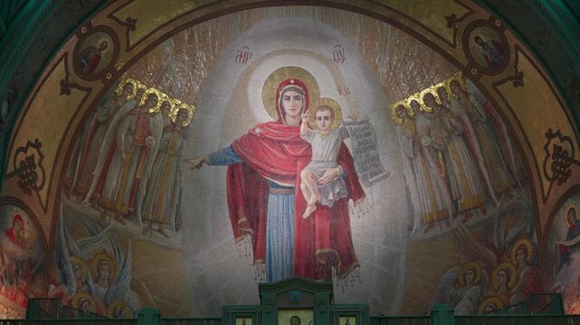 Orthodox Madonna and Child icon dominates richly decorated church interior, emphasizing sacred architecture and surrounding saints. Central religious mural remains framed by arches and iconostasis.