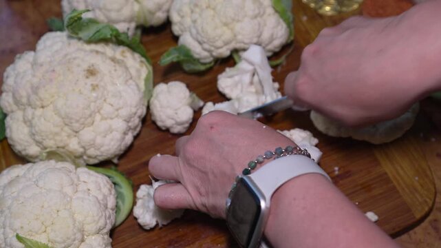 Cauliflower food preparation, woman cuts fresh organic vegetable on wooden cutting board, preparing healthy plant based vegan meal in home kitchen