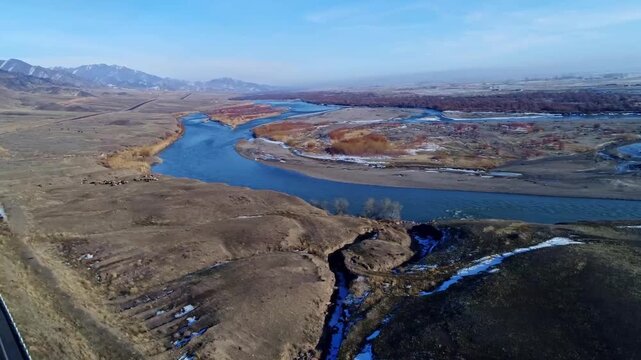 Aerial view of the Tarim River winding through arid steppe landscape with distant snow-capped mountains in Xinjiang, China