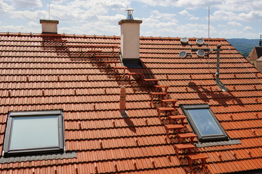Tiled roof with a ladder leading to the chimney on a sunny day, roof maintenance.