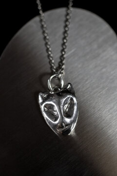 A silver pendant shaped like a cat's face hangs from a delicate chain. The background is softly blurred, highlighting the jewelry's intricate design.