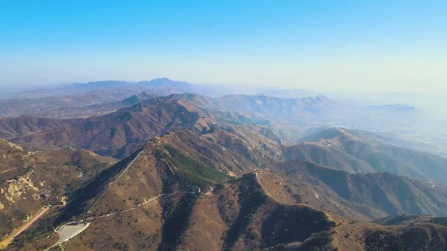 Aerial view of ancient stone wall snaking across rugged mountain ridges in Henan Province, China under clear blue sky