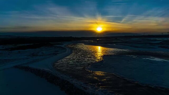 Sunset over the Ili River in Xinjiang winter landscape, aerial timelapse with golden reflection on icy water and snow-dusted banks