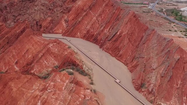 Aerial drone view of a wooden walkway winding through the red sandstone cliffs of Tian Shan Grand Canyon in Kuqa, Xinjiang