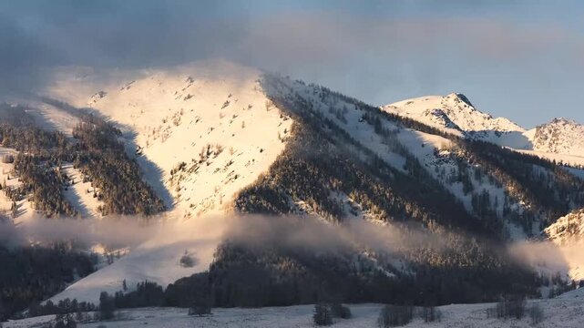 Snow-covered mountain range in Xinjiang during winter sunrise with mist rolling through valleys