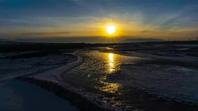 Ili River in Xinjiang at winter sunset with icy banks and golden reflection, aerial timelapse