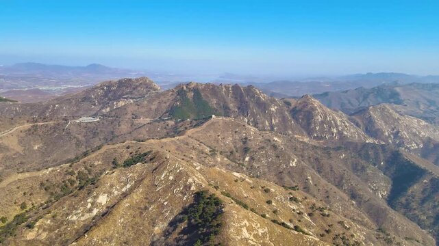Aerial drone view of ancient stone wall ruins winding across rugged mountain ridges in Qifeng Mountain, Henan, China under clear blue sky