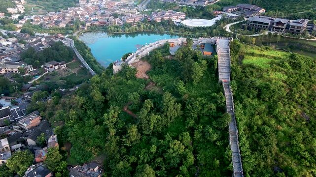 Aerial drone view of Qingyan Ancient Town with traditional Chinese architecture, stone walkway winding up a forested hill, and turquoise lake surrounded by historic buildings